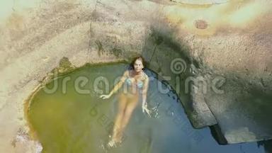 令人放松的女人沐浴在透明的河面上。 年轻女子在背景大石头上的河水中游泳